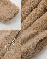 A beige teddy jacket made of soft fleece, featuring a high collar, modeled with a close-up showing part of a hand wearing a fashion accessory, emphasizing the jacket's plush texture.