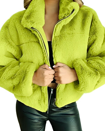 
A beige teddy jacket for women made of soft fleece material, featuring a zip-up front and a high collar, shown in a large size. The jacket is complemented by green elements and is displayed with an outstretched hand to show the sleeve and texture details. The background is white, providing contrast to the jacket's color.