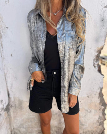 Damen Metallic Silber Blazer mit a fashion-forward design, featuring a shiny metallic silver finish. The blazer has structured shoulders, a classic collar, and long sleeves, exuding elegance and sophistication ideal for party settings. The grey hue complements the metallic sheen, making it a standout piece in women's outerwear.