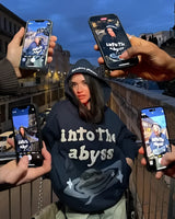 Oversized blue camouflage hoodie worn by a person outdoors, showcasing the sleeve design, with a hand holding a mobile phone and wearing sunglasses.