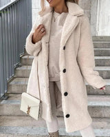 
A woman wearing a long brown teddy coat styled for winter, showcasing its fashionable design with an apricot hue in an XXL size. The coat features a collar and long sleeves, standing out with its outerwear appeal.