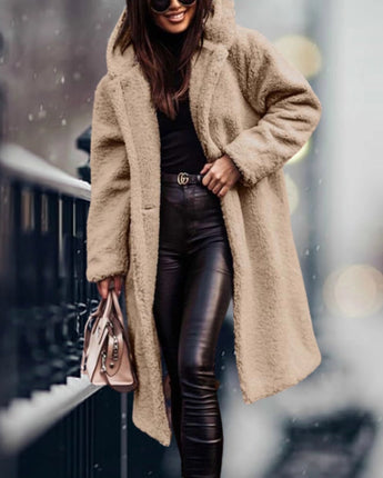 
A woman wearing a long blue teddy coat, characterized by its fluffy texture, suitable for winter fashion. The coat features long sleeves and extends to the knee, offering a cozy and stylish look. The woman is also wearing eyewear, adding a fashionable touch to her outfit.