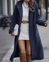 
Woman wearing a long, fluffy blue teddy coat in a deep navy color, styled for winter. The coat features a soft, textured fabric with long sleeves and a comfortable fit, reaching below the knees.
