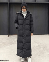 Frau trägt langen schwarzen Daunenmantel, oversized Maxi Winterjacke; Mantel hat lange Ärmel und hohen Kragen.