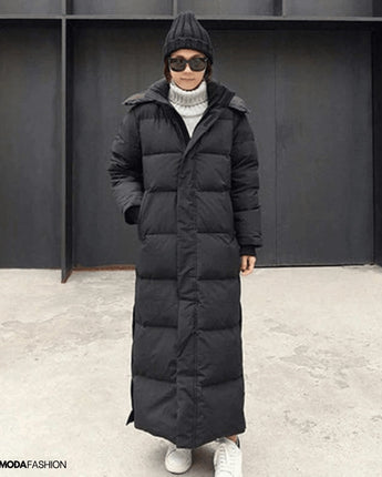 Frau trägt langen schwarzen Daunenmantel, oversized Maxi Winterjacke; Mantel hat lange Ärmel und hohen Kragen.